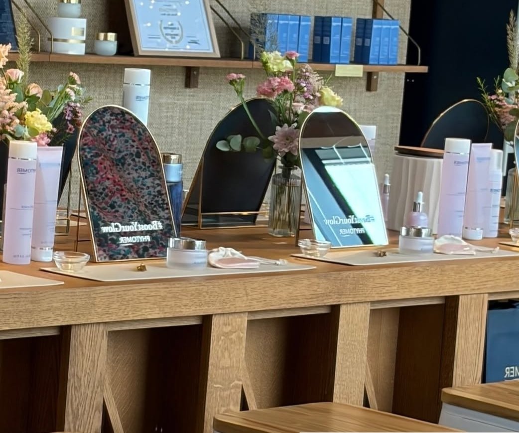Table de soins ou de maquillage avec miroirs, produits de beauté, fleurs, et matériel de beauté sur fond d'étagère et décorations.