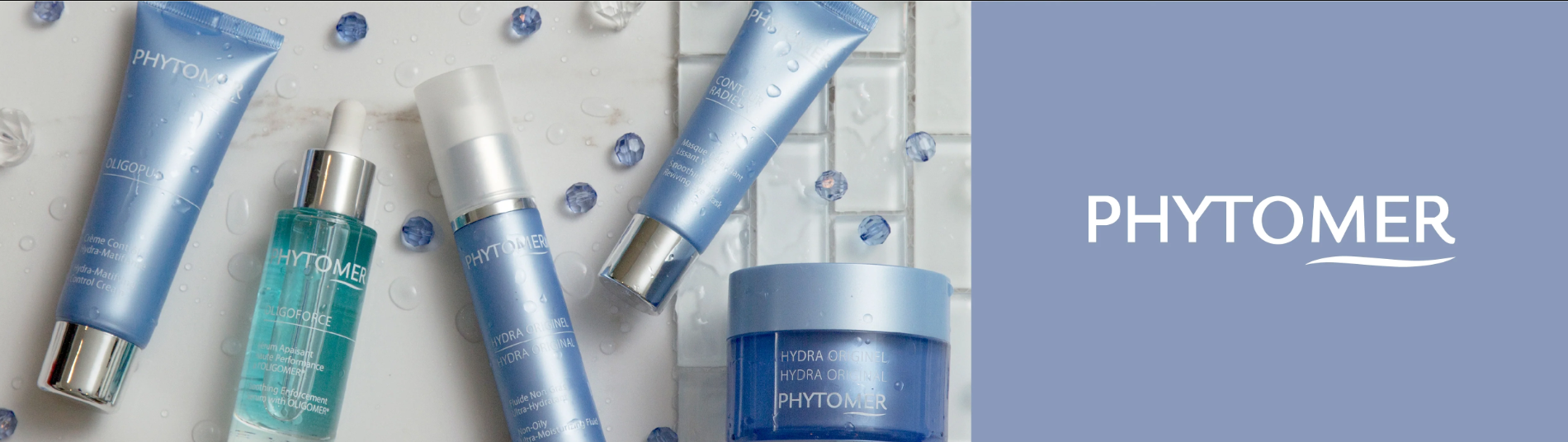 Assortiment de produits de soins de la peau PHYTOMER, comprenant des crèmes, sérums et masques dans des emballages bleus et transparents, avec quelques gouttelettes d'eau en décor.