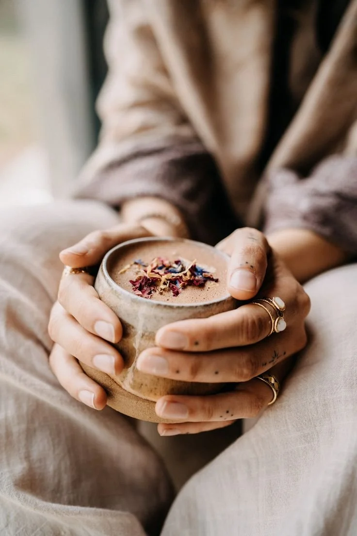 Une personne tient une tasse en céramique contenant une boisson chaude décorée de fleurs séchées.