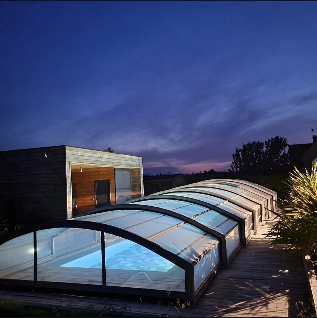 Piscine couverte dans une maison moderne en bois, sous un ciel crépusculaire