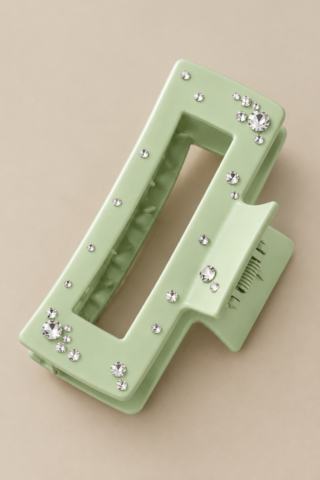 Light green hair clip decorated with scattered clear rhinestones, photographed on beige background.