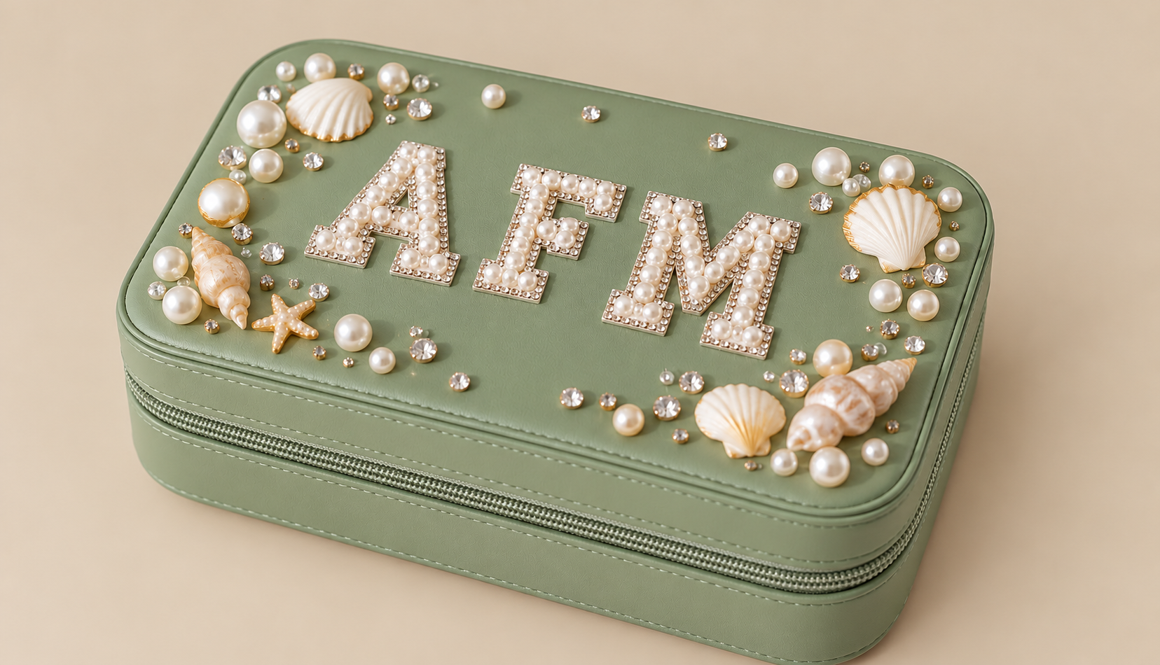 A green jewelry box decorated with seashells, pearls, and rhinestones, with the word "AEM" spelled out in pearl-studded letters on top.