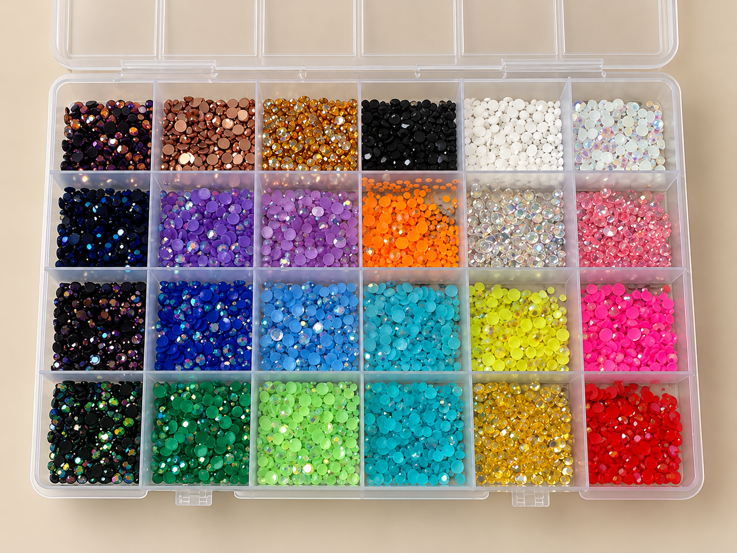 A clear plastic organizer box filled with small, colorful rhinestones arranged in separate compartments. The rhinestones are in various colors including purple, blue, green, yellow, orange, pink, black, white, and gold.