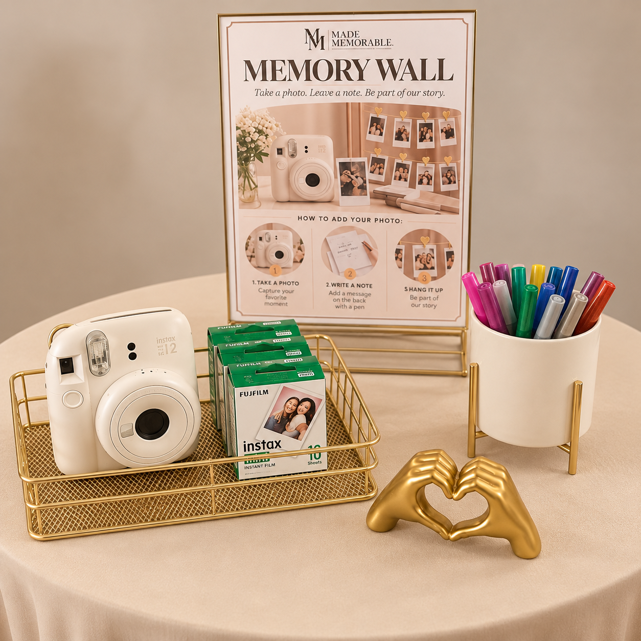 A photo of a memory wall station with a fun display, featuring a white instant camera, several boxes of Fujifilm Instax instant film, and a white cup holding colorful markers. Behind the setup is a printed instruction sign showing how to create a mem