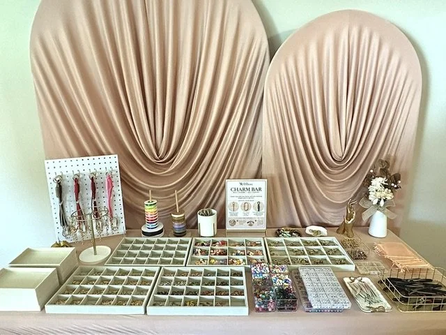 A curated charm bar with gold jewelry trays, decorative charms, and keychain-making supplies for guests.