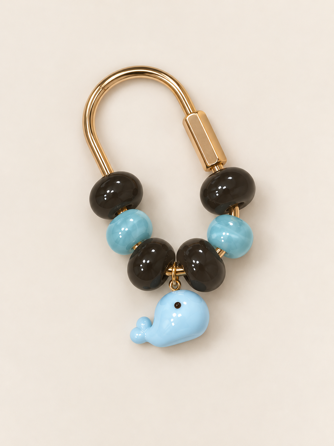 A decorative keychain featuring alternating black and light blue beads with a smiling light blue whale charm hanging at the bottom, attached to a gold-colored metal ring.