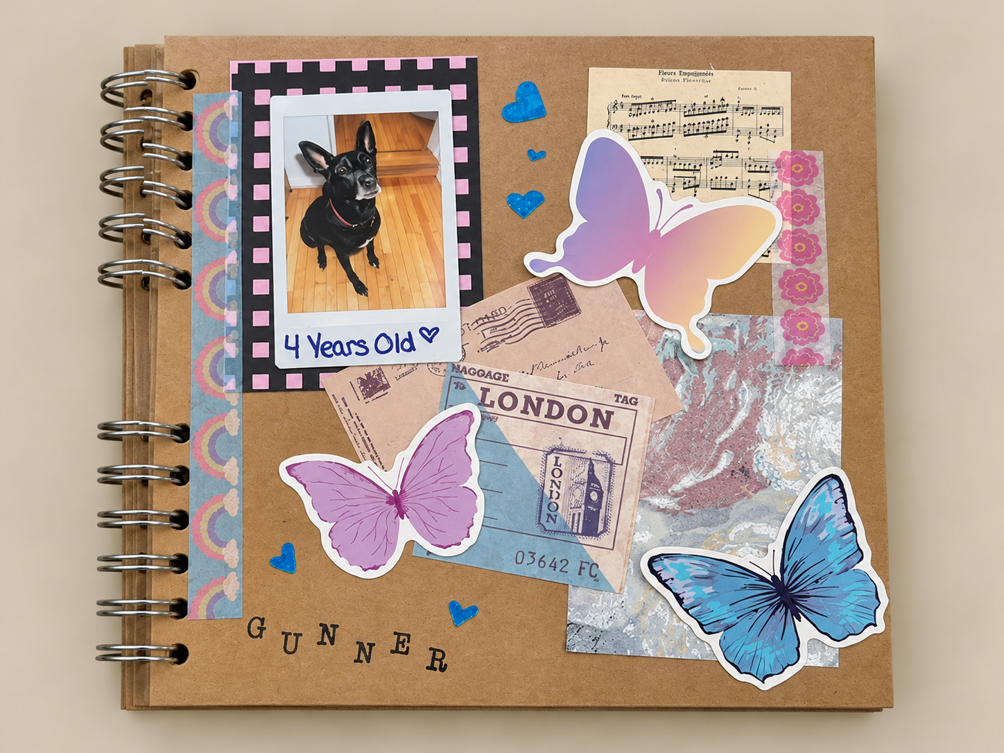 A scrapbook page featuring a photo of a black dog with upright ears, labeled '4 Years Old'. The page is decorated with colorful butterfly stickers, travel-themed items like a London ticket, and various decorative papers and washi tapes.