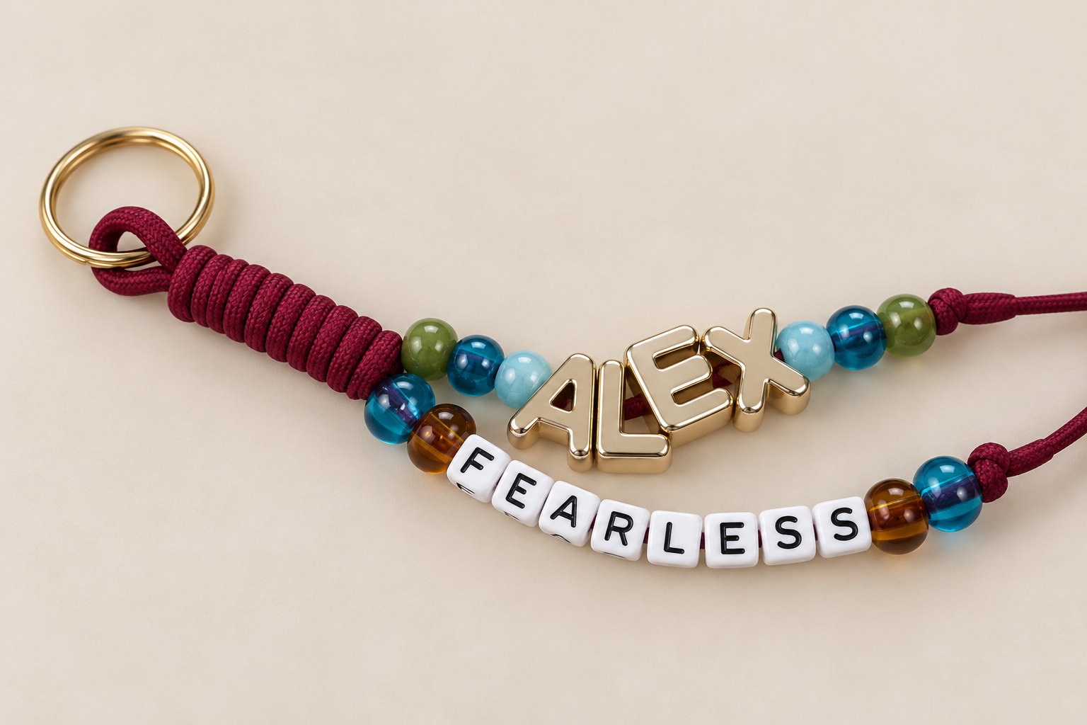A keychain with beads, a gold letter 'ALEX' pendant, and white beads spelling 'FEARLESS,' on a neutral background.