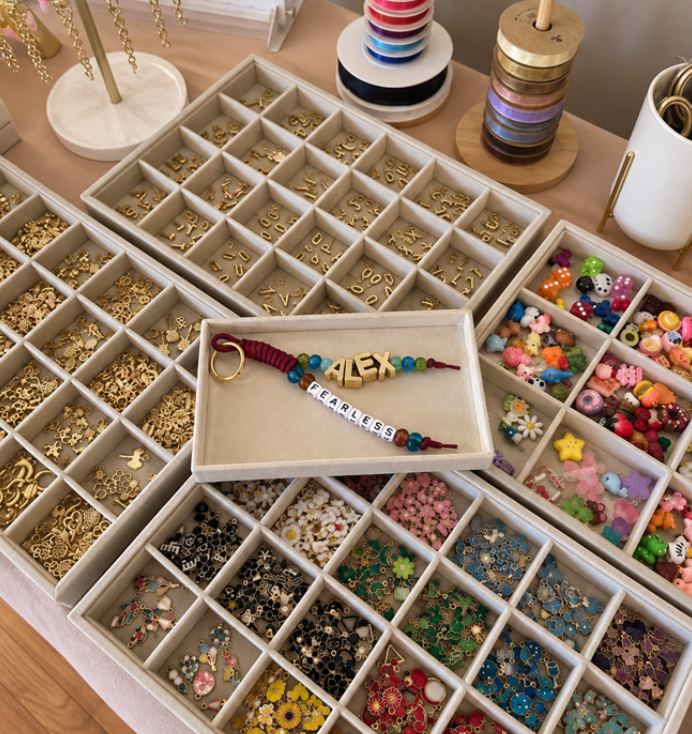 Jewelry organizer with colorful beads, charms, and alphabet letter beads, including a bracelet spelling 'ALEX' and 'FEARLESS'.