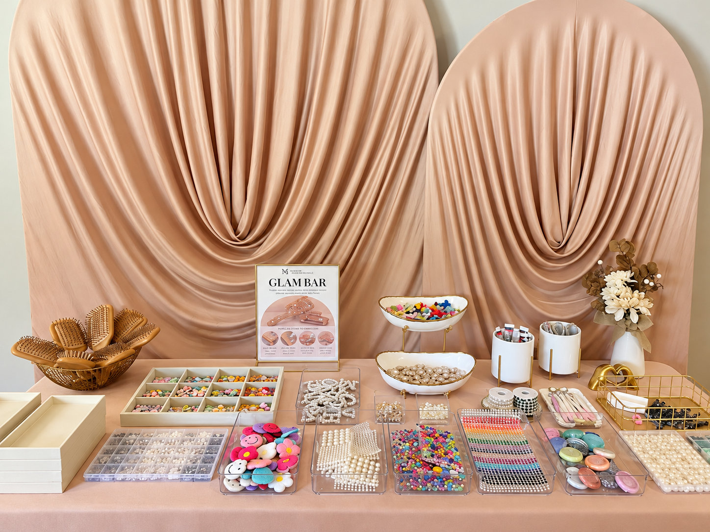 A display of jewelry and accessories on a pink table, with organized beads, buttons, and decorative items, in front of a draped pink backdrop.