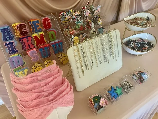 Display of colorful hair accessories, jewelry, and decorative pins on a table, with bowls containing small items and a collection of pink headbands.