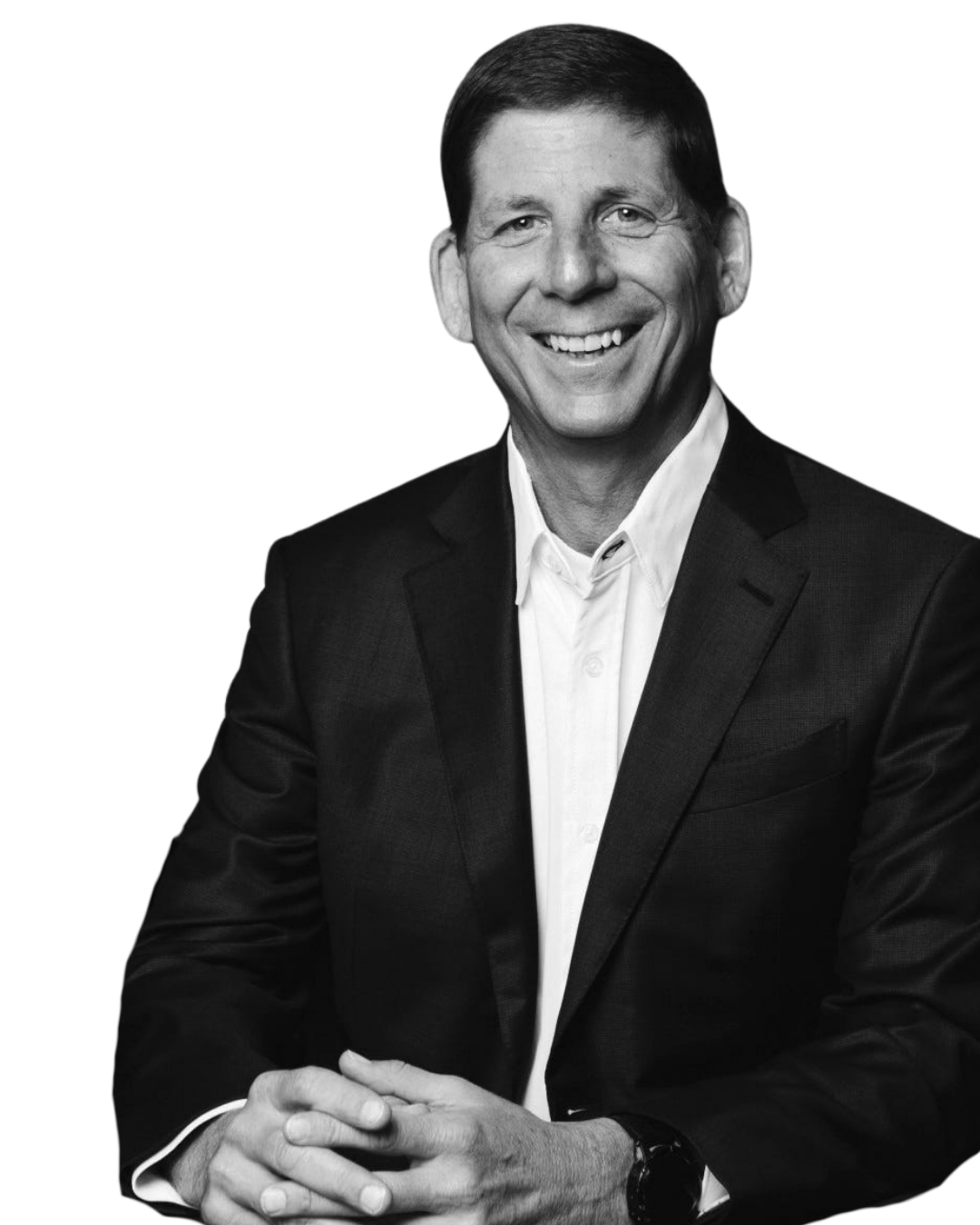 A black-and-white photo of a smiling man in a suit and white shirt, with short dark hair, sitting with his hands clasped.