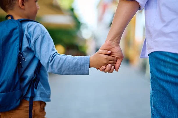 A child holding an adult's hand while walking outside.