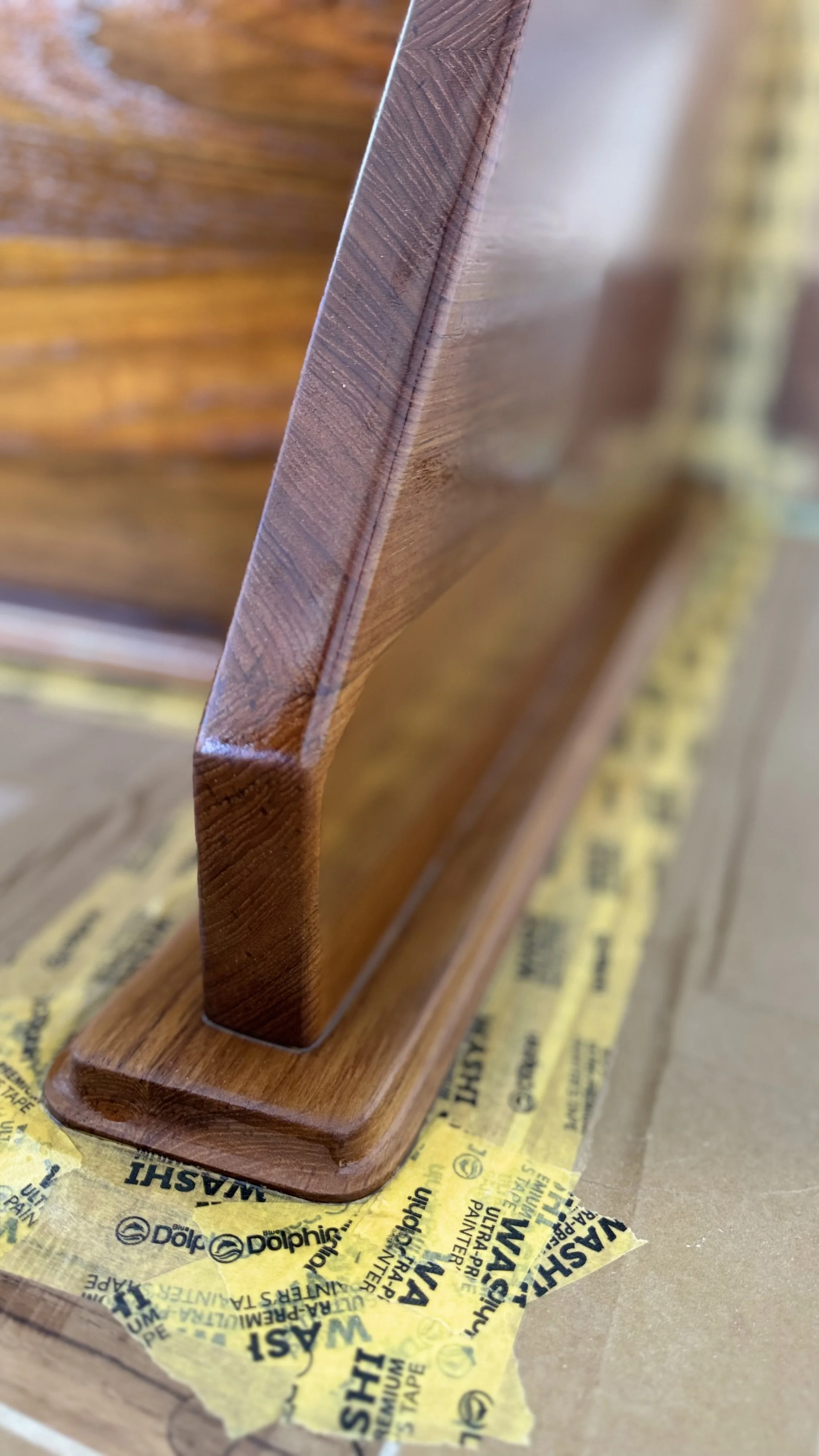 Close-up of a wooden picture frame with masking tape underneath, resting on a cardboard surface.