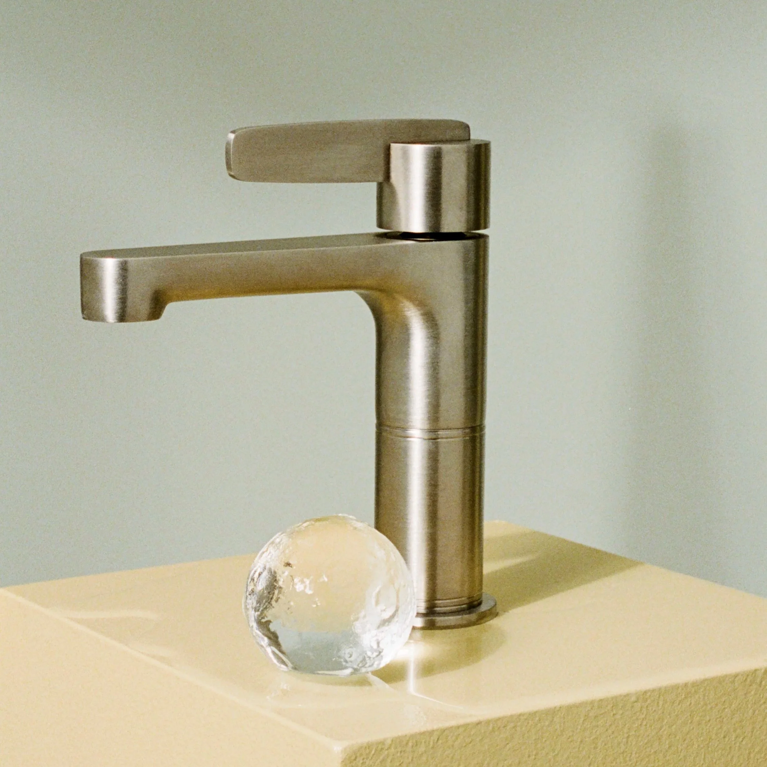 Close-up of a modern brushed nickel bathroom faucet with a single handle inspired by art-deco style.