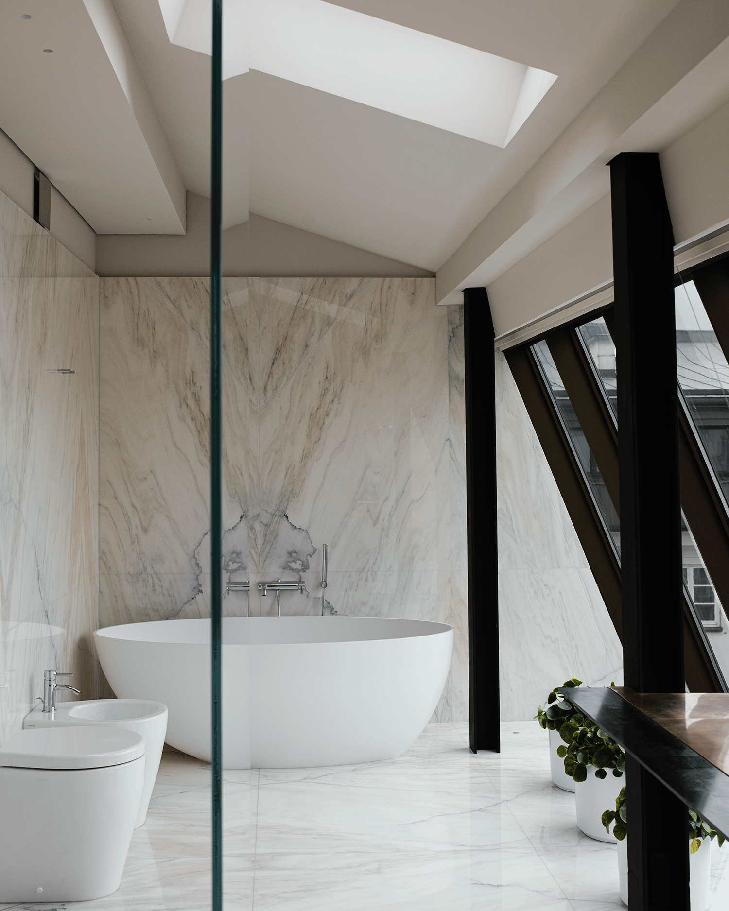 Modern bathroom in Hotel Pod Różą in Kraków with freestanding bathtub, bidet, marble walls, large skylight, and black window frames.