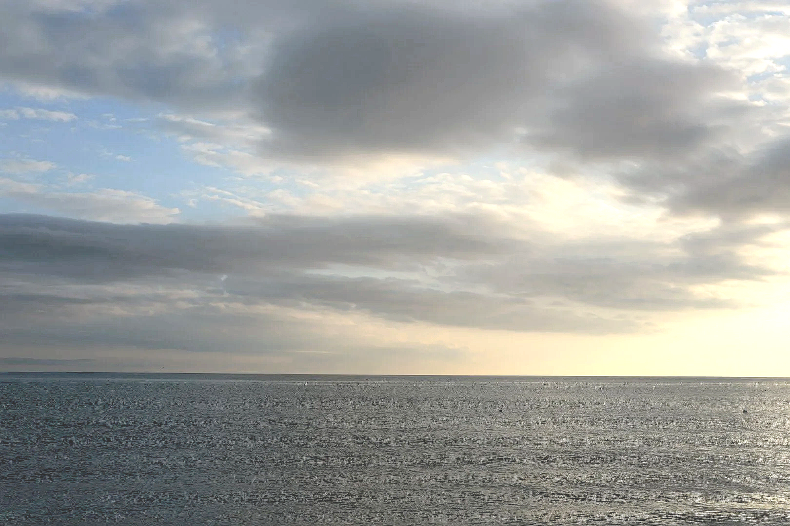Overcast sky with clouds over a calm body of water, likely a lake or ocean, with some sunlight breaking through the clouds.