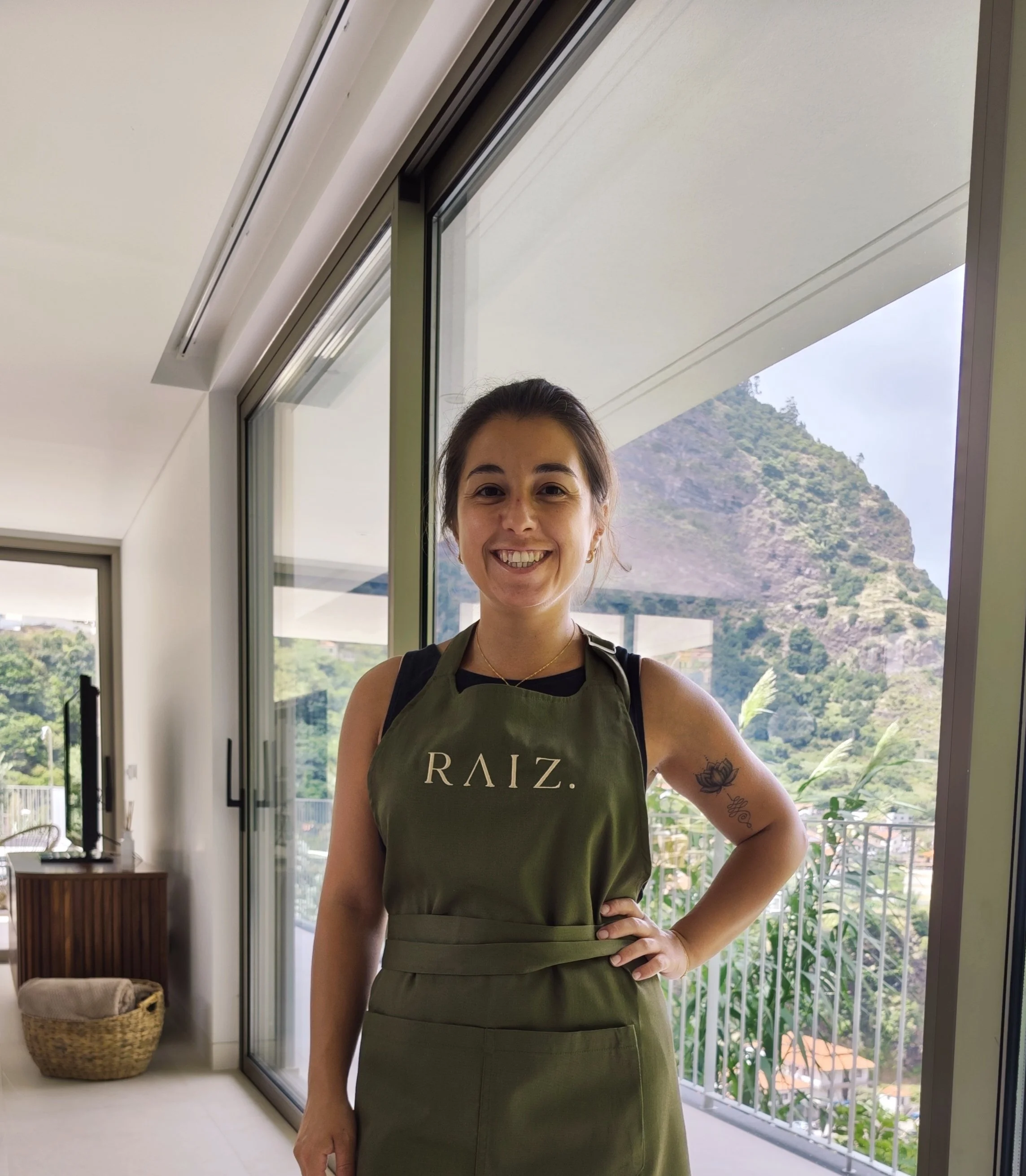 Woman wearing a RAIZ. apron beside a window overlooking the mountains
