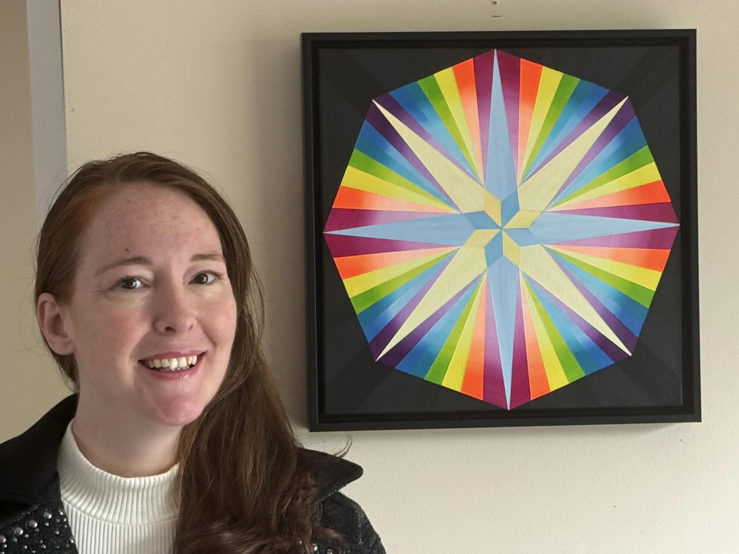 Elithia smiling in front of a framed, colorful geometric artwork on a beige wall.