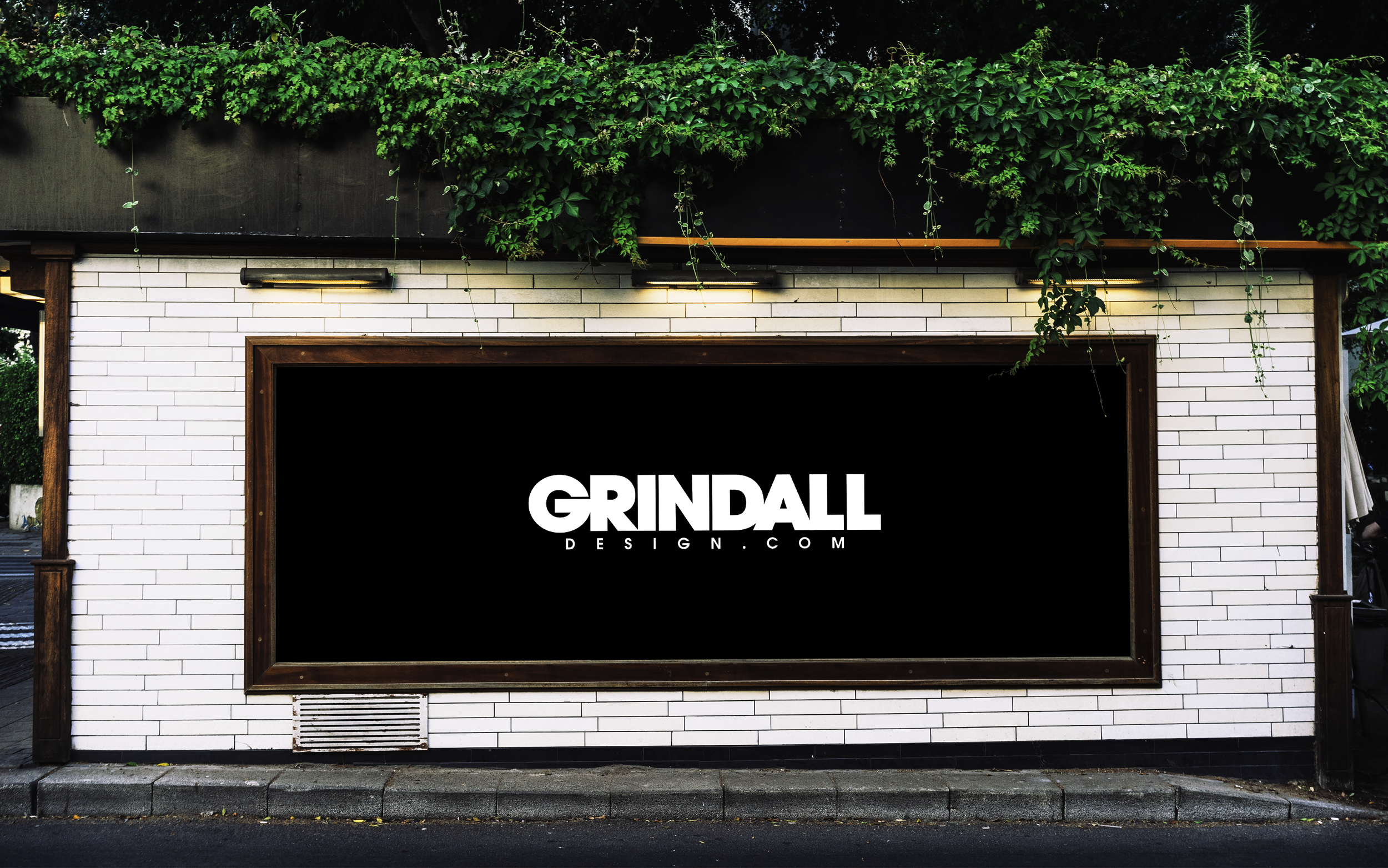 Outdoor restaurant facade with white brick walls, lush green vines, and a black sign reading “GRINDALL DESIGN.COM.”