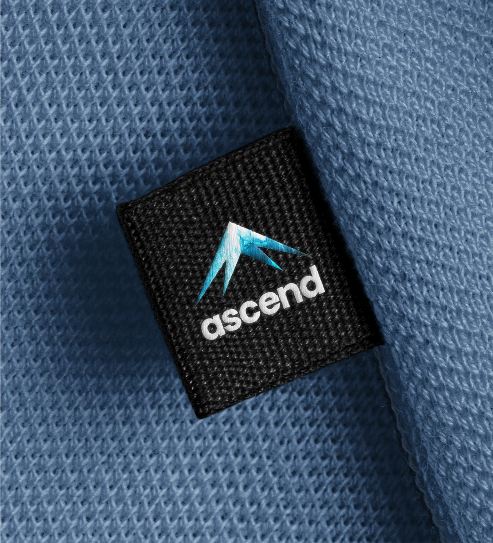 Black woven fabric label with a blue stylized logo and white “ascend” text on blue knit fabric.