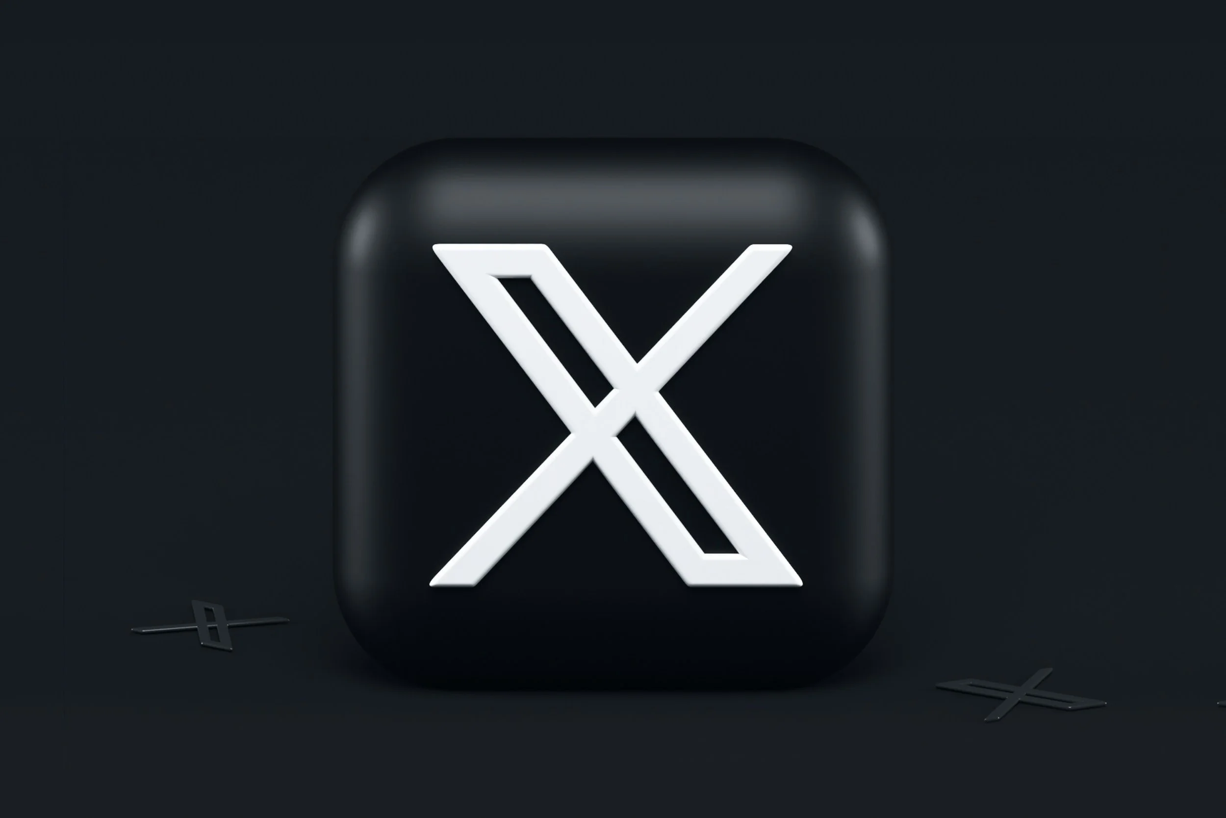 A black device with a white illuminated logo in the shape of a stylized 'X' in the center, surrounded by scattered black and silver letters and symbols on a dark background.