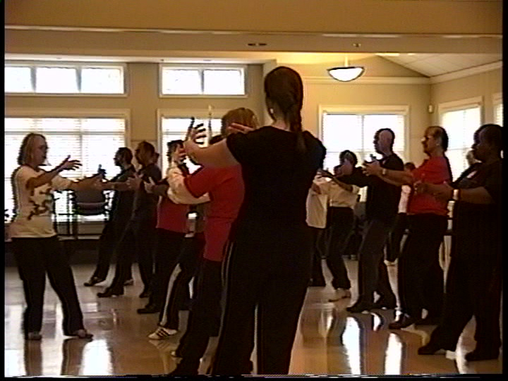 Group of women practicing dance in a brightly lit studio with wooden floors and large windows.