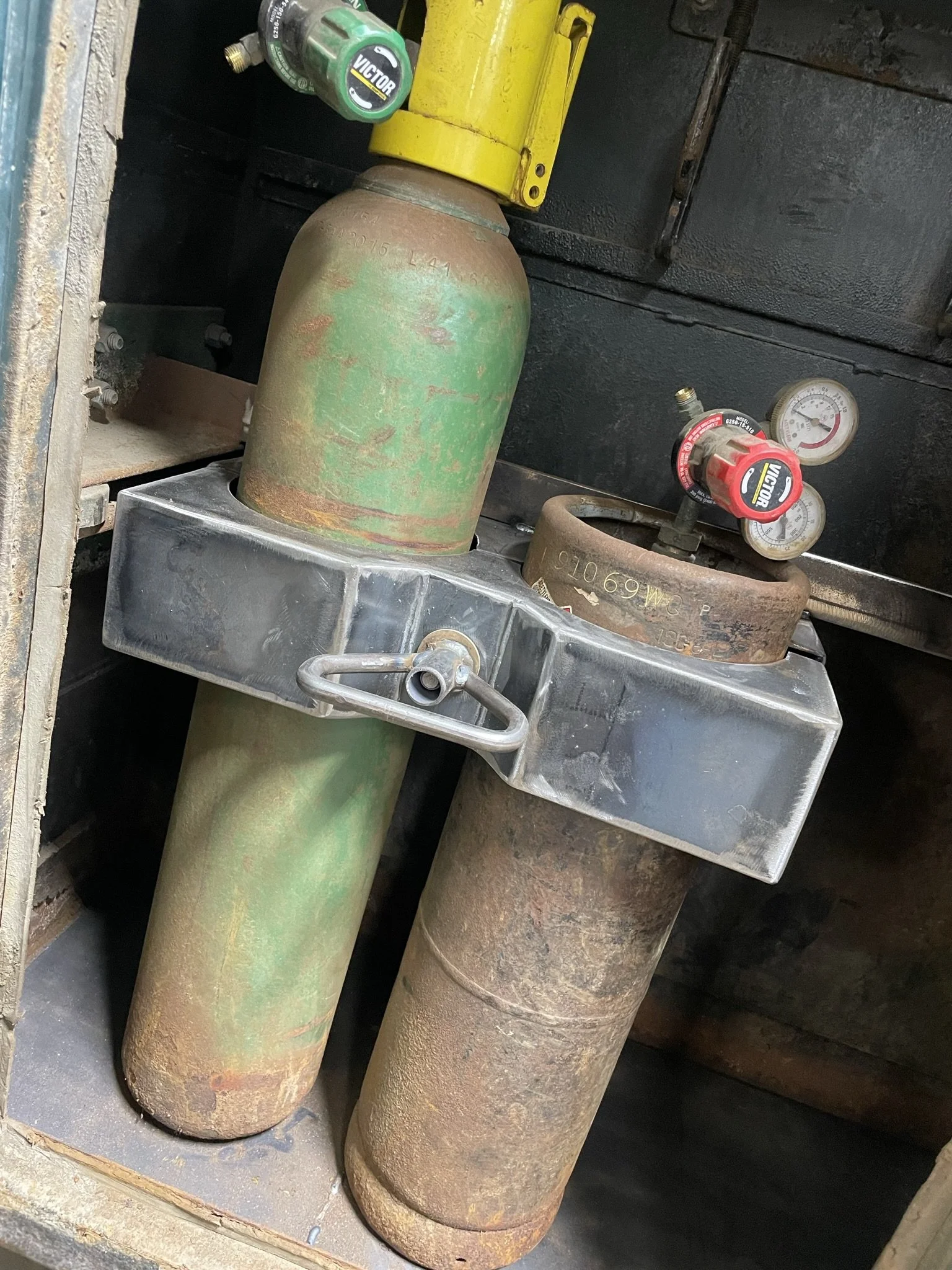 Four large old rusted gas cylinders in a metal cart with gauges and valves, possibly used for welding or industrial purposes.