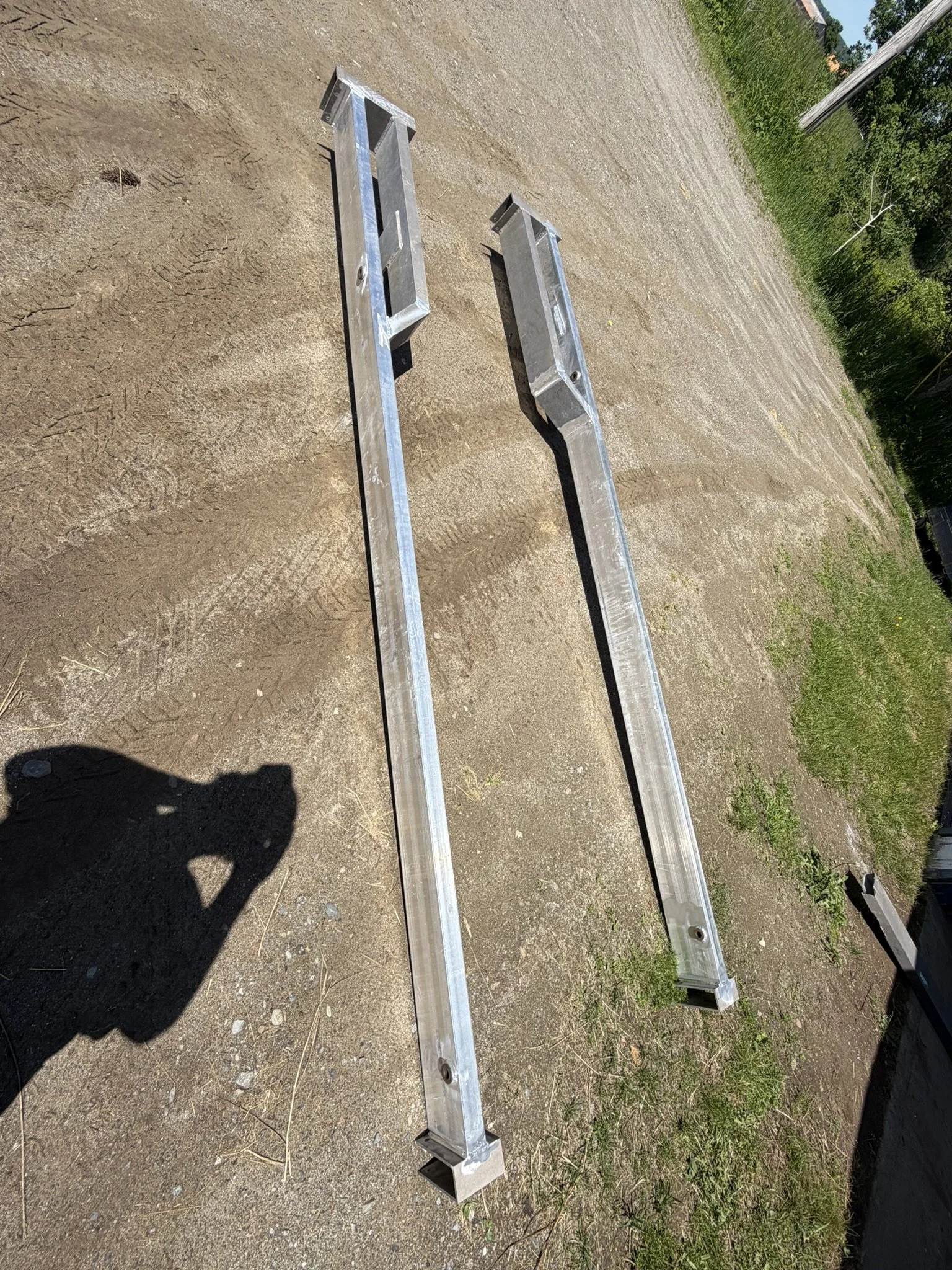 Two metal lengths of roof racking lying on dirt ground in an outdoor setting.