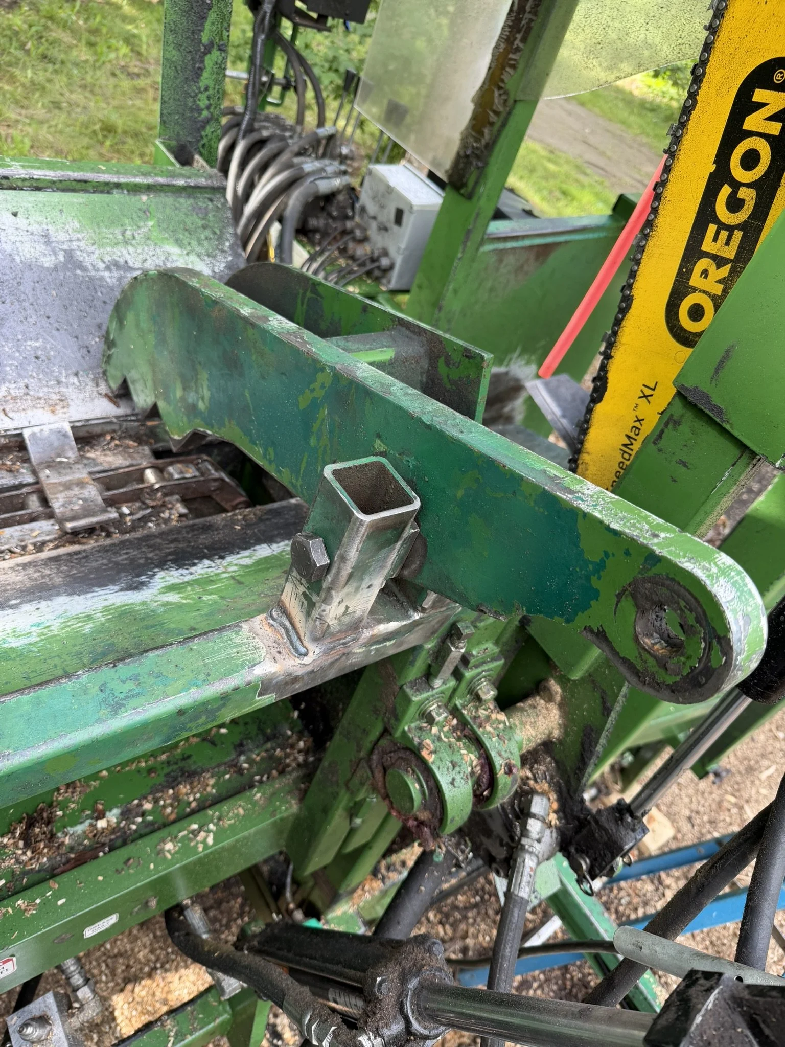 Close-up of the mechanical parts and gears of a green agricultural machine, showing chains, levers, and metal components.