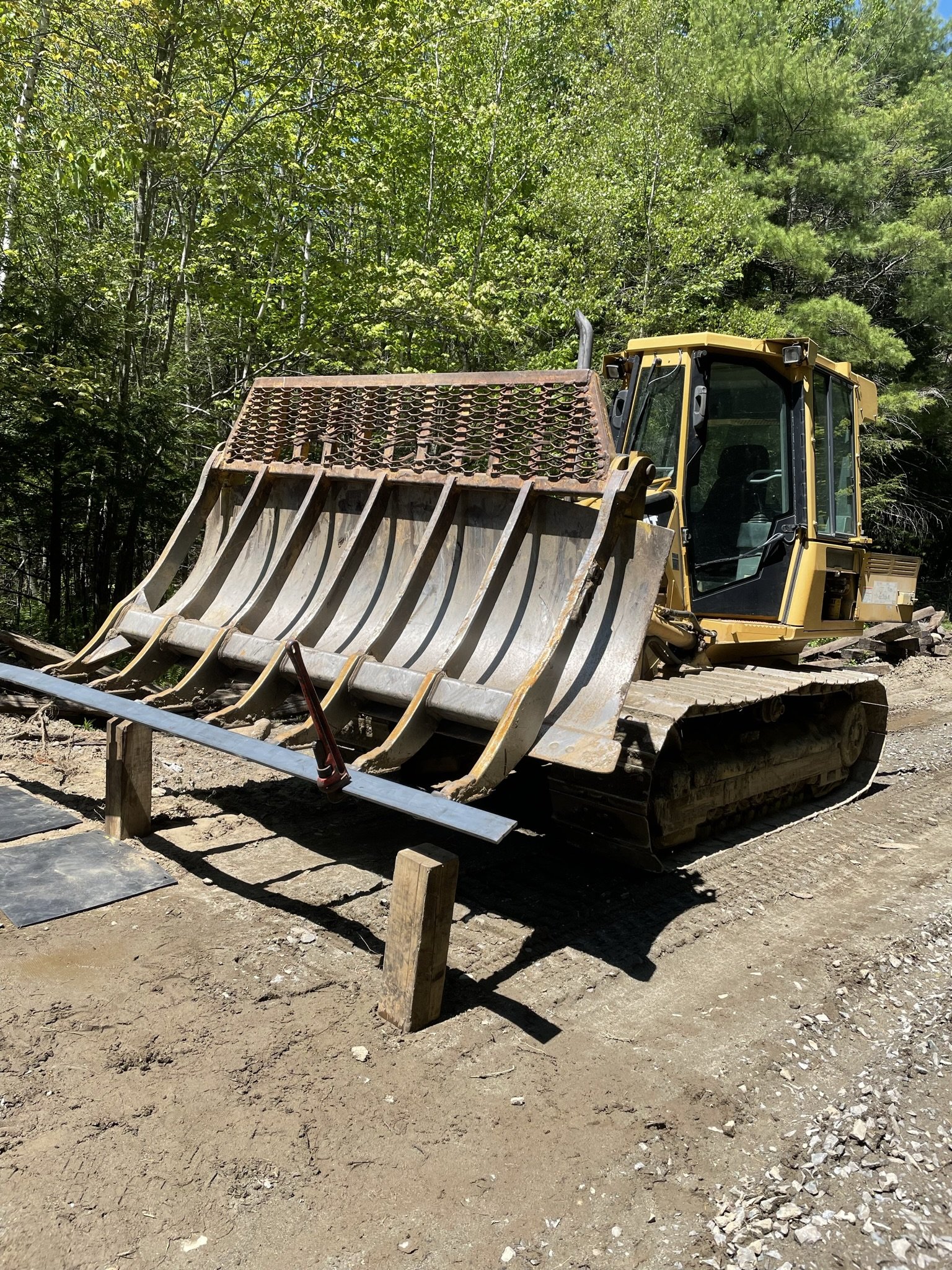 A yellow bulldozer on a dirt construction site surrounded by trees and green foliage.
