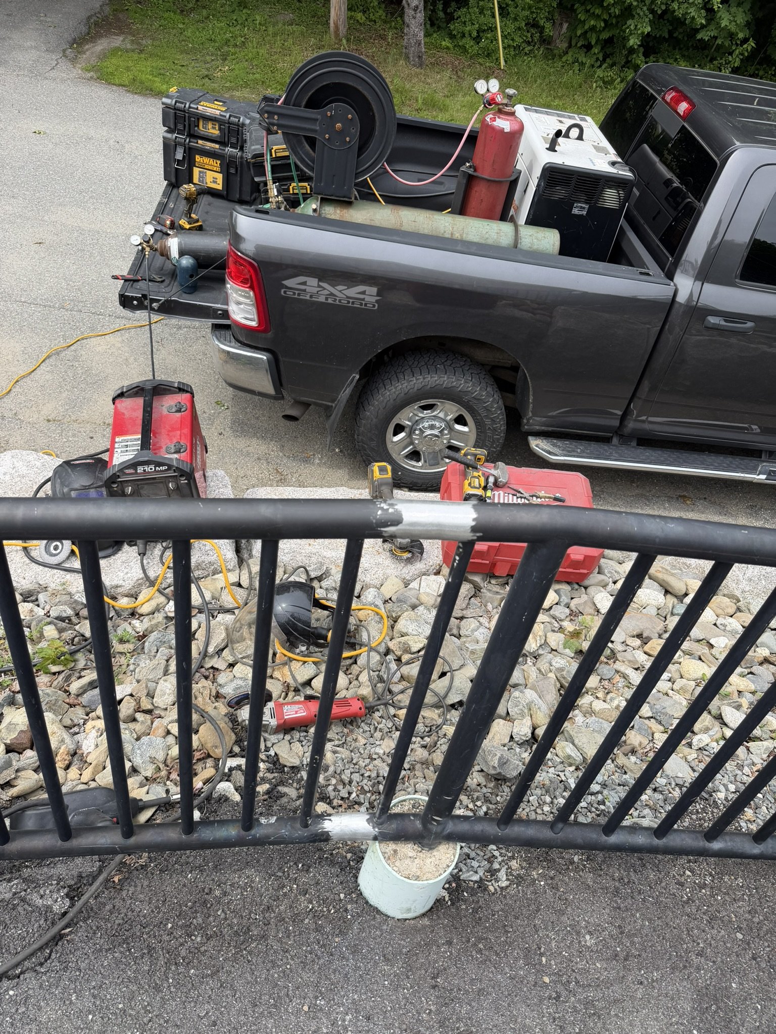 Pickup truck with equipment including a fire extinguisher, generators, tools, and hoses in the truck bed, viewed from above through a black metal fence.