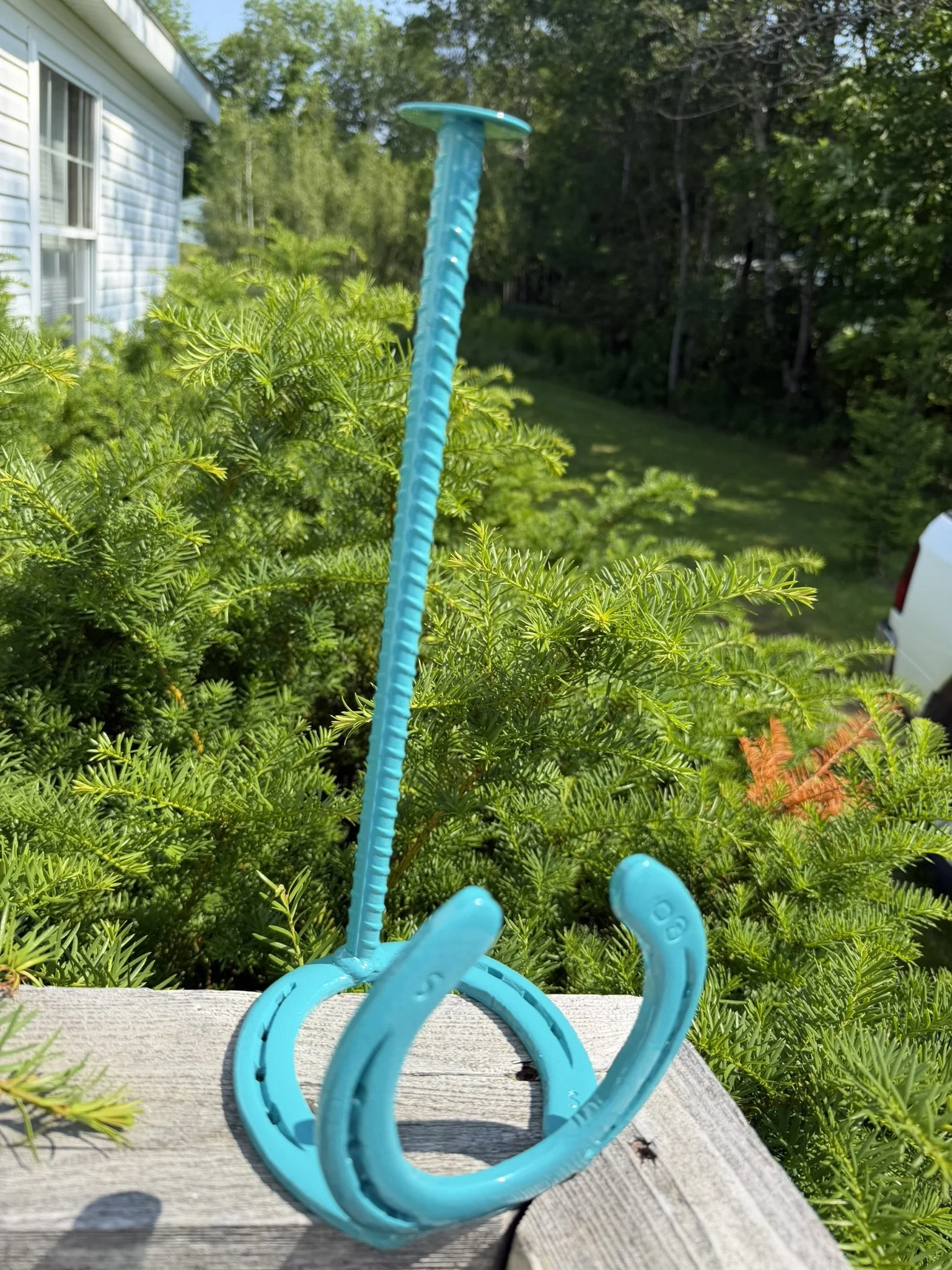 Blue plastic toy with long tentacle-like extensions resting on a weathered wooden surface outdoors, with green plants and trees in the background.
