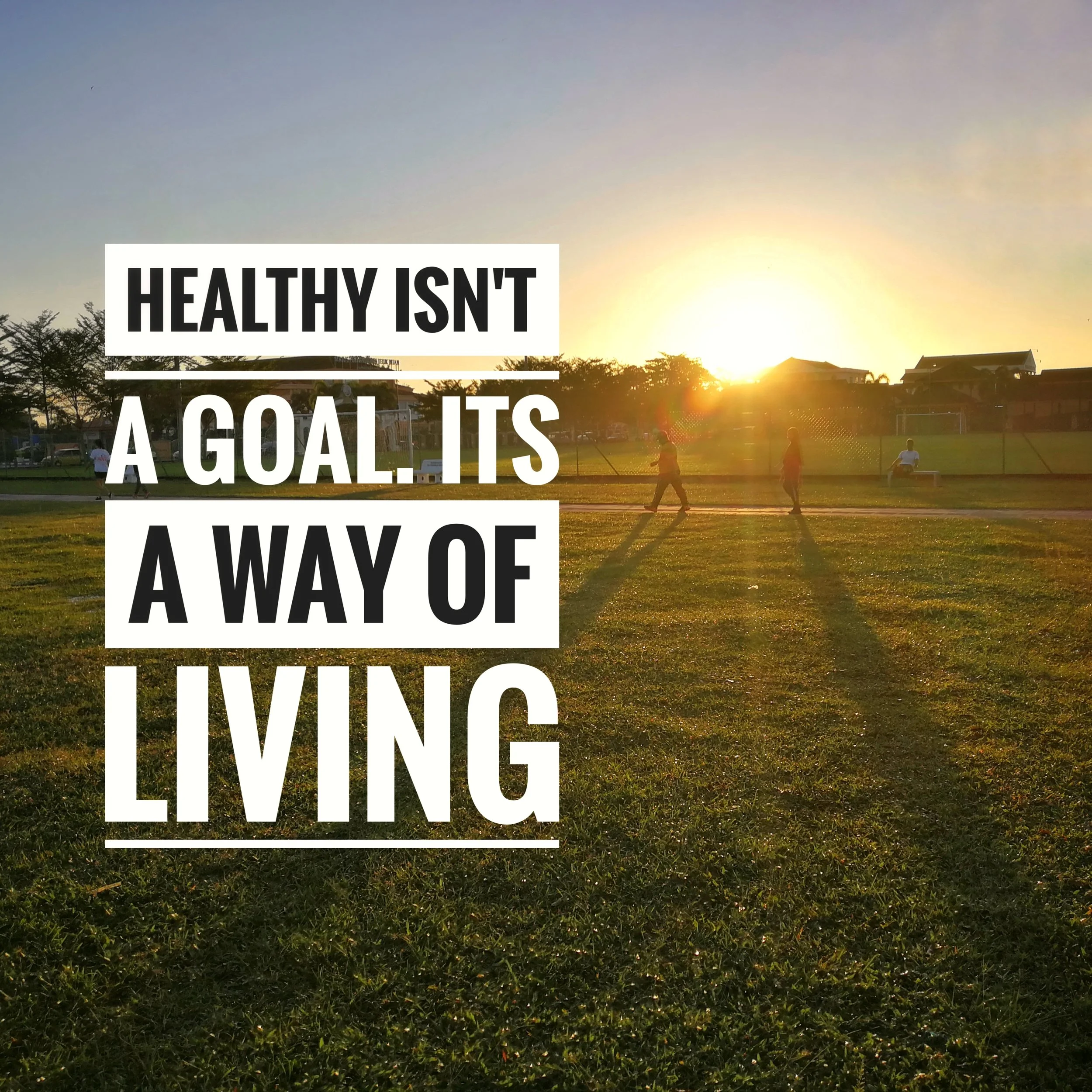 A grassy park at sunset with people walking and playing, and a large overlay text that reads 'HEALTHY ISN'T A GOAL, IT'S A LIFESTYLE.'