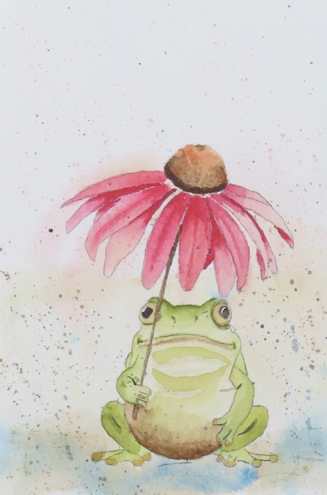 Watercolor painting of a green frog holding a pink flower, with a brown center, above its head. The background is white with colorful speckles.
