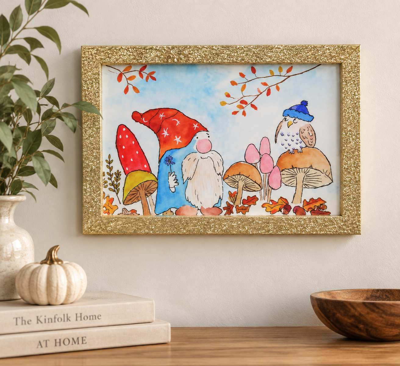 Framed Enchanted Autumn watercolor art featuring a gnome, owl, mushrooms, and colorful fall foliage displayed on a wall.