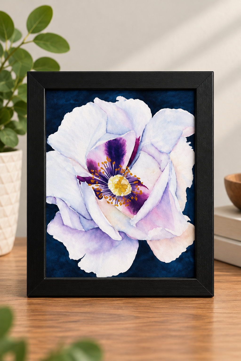 Watercolor print of a delicate white, lavender, and blush flower with a vibrant purple and gold center against a deep navy background, displayed in a black frame