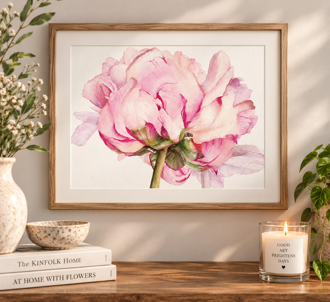 Pink peony watercolor print in a natural wood frame with a white mat, styled on a warm neutral wall with botanical home décor.