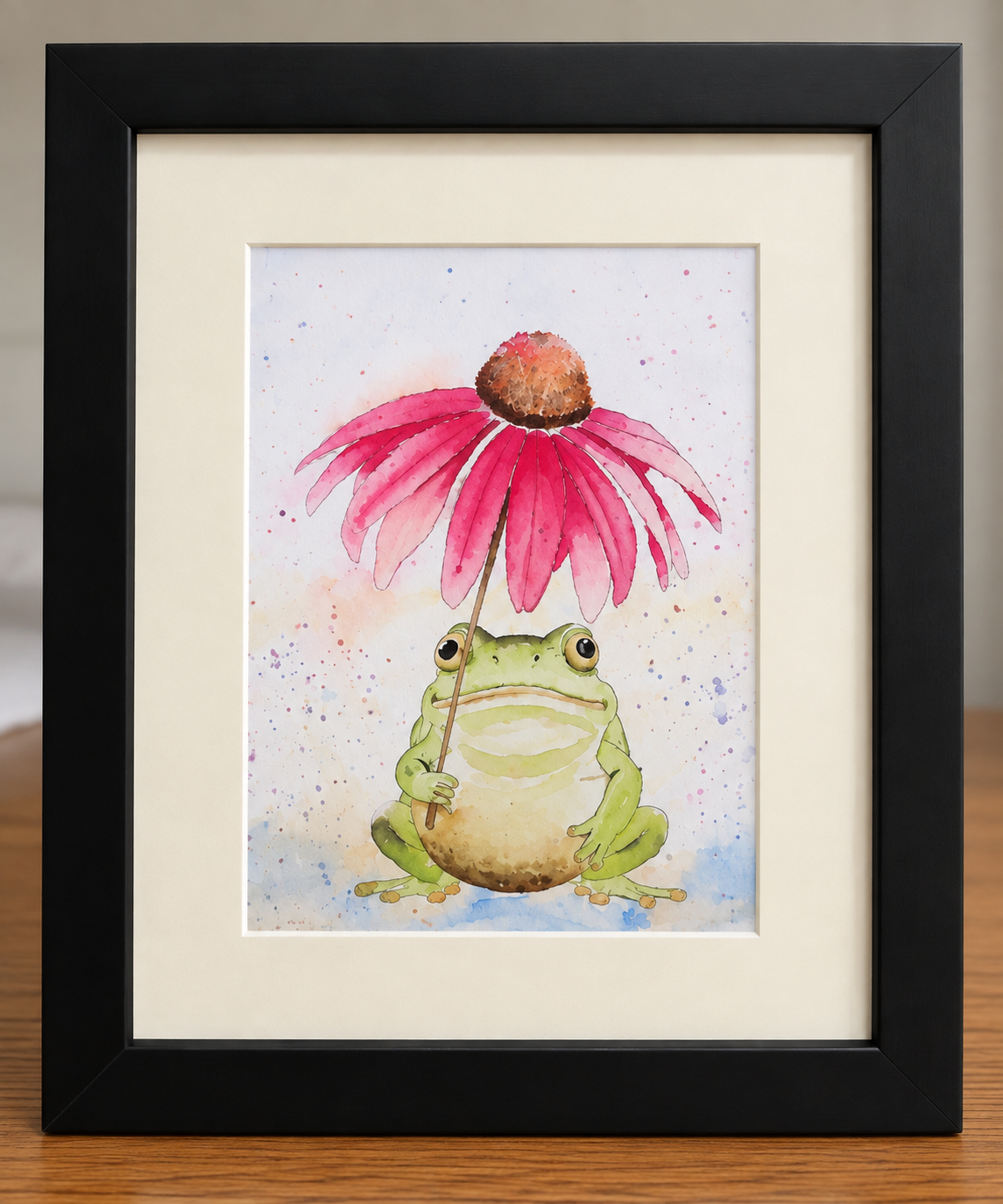 Close-up of the framed Under the Coneflower watercolor print showing a whimsical green frog beneath a pink coneflower with colorful watercolor splatters.