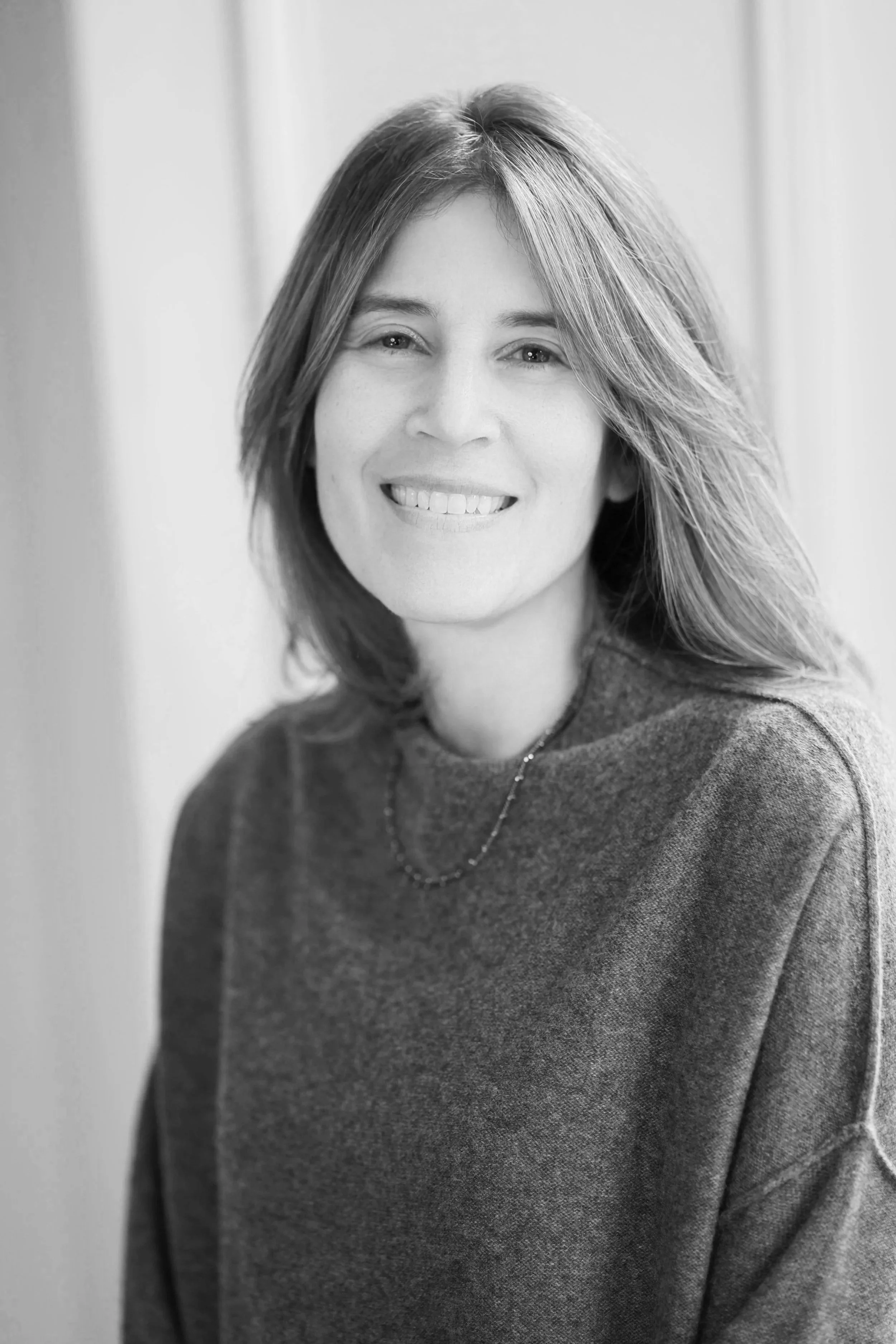 Black and white portrait of a woman with shoulder-length hair, smiling, wearing a sweater and a necklace.