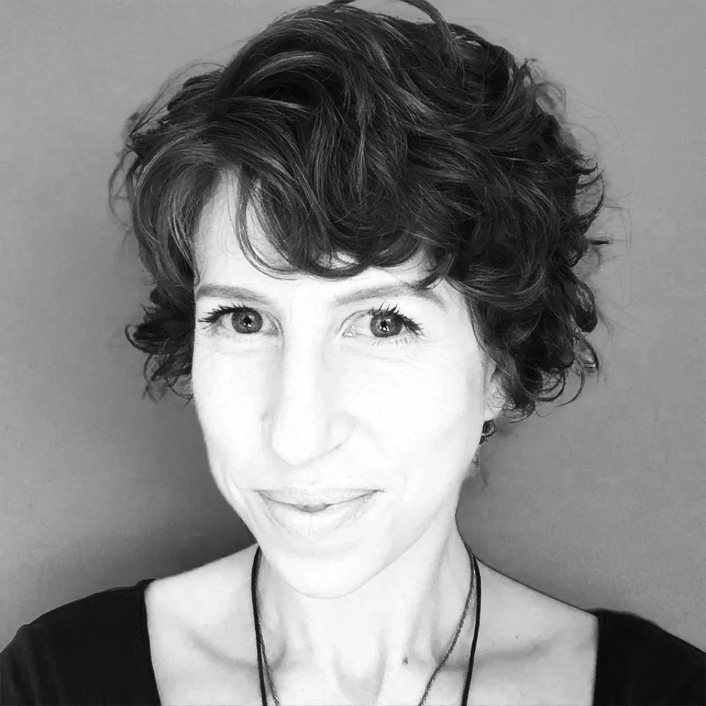 Black and white portrait of a woman with short, curly hair, smiling, wearing a dark top and a necklace.
