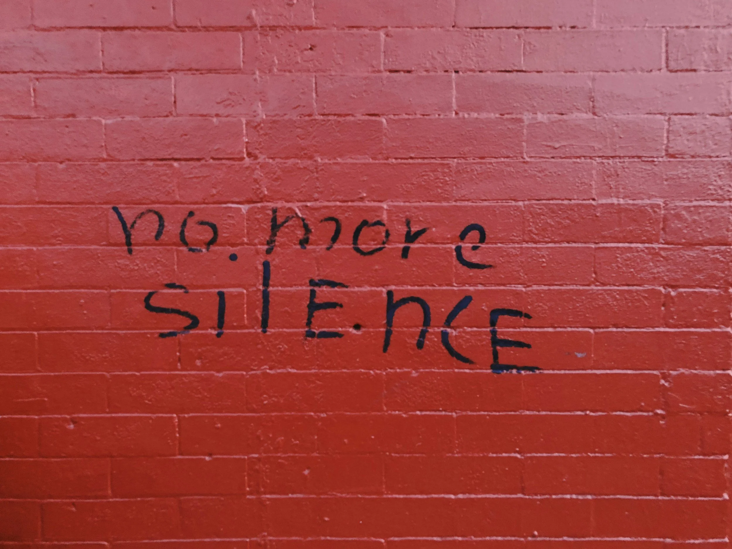 Red brick wall with handwritten black text.