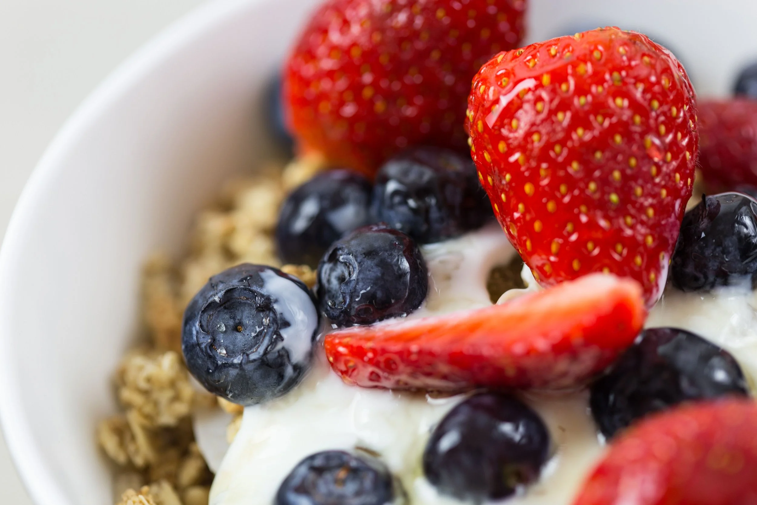 Close-up of a bowl with strawberries, blueberries, and granola, topped with yogurt.