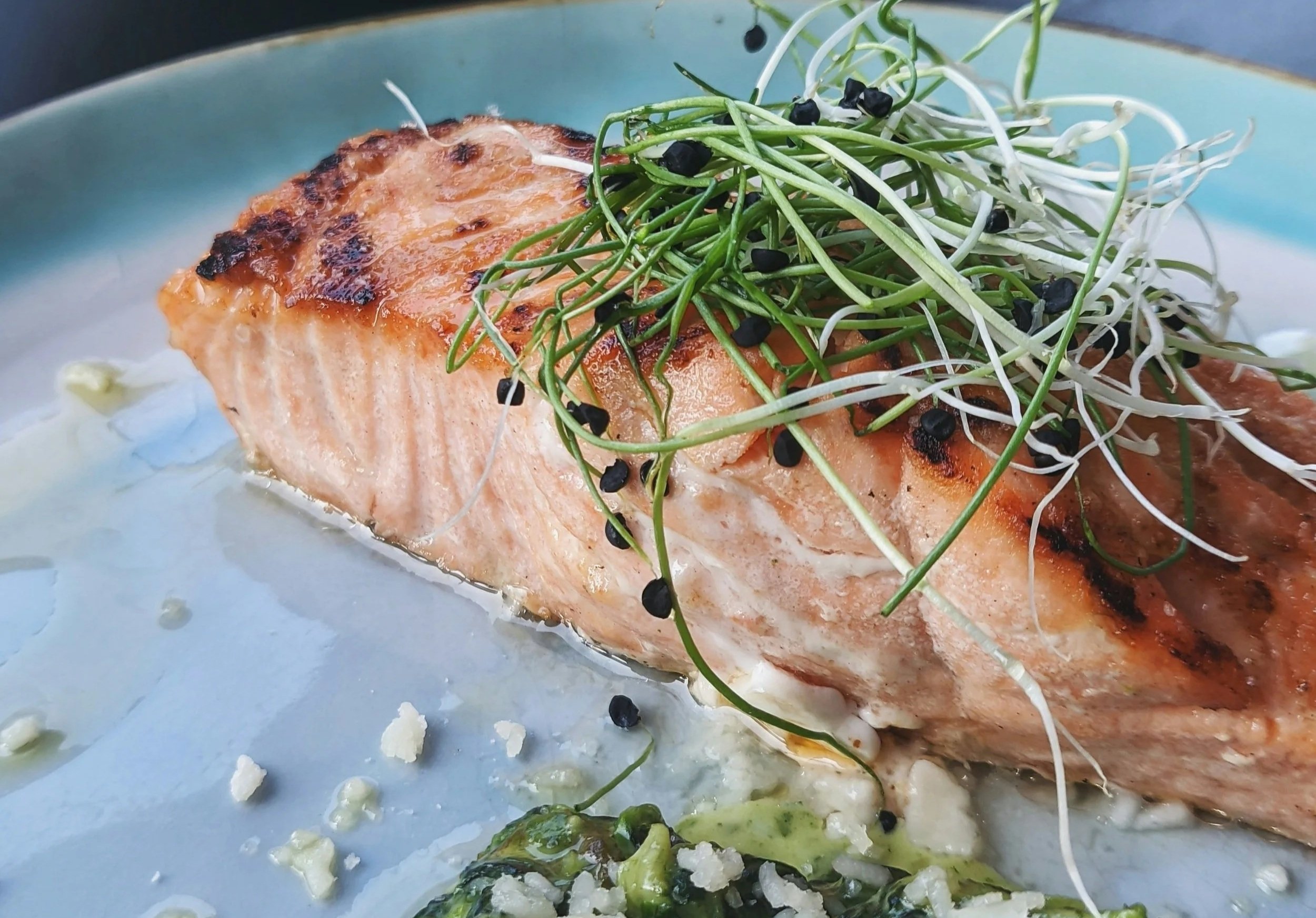 Cooked salmon fillet topped with microgreens and black sesame seeds on a light blue plate.
