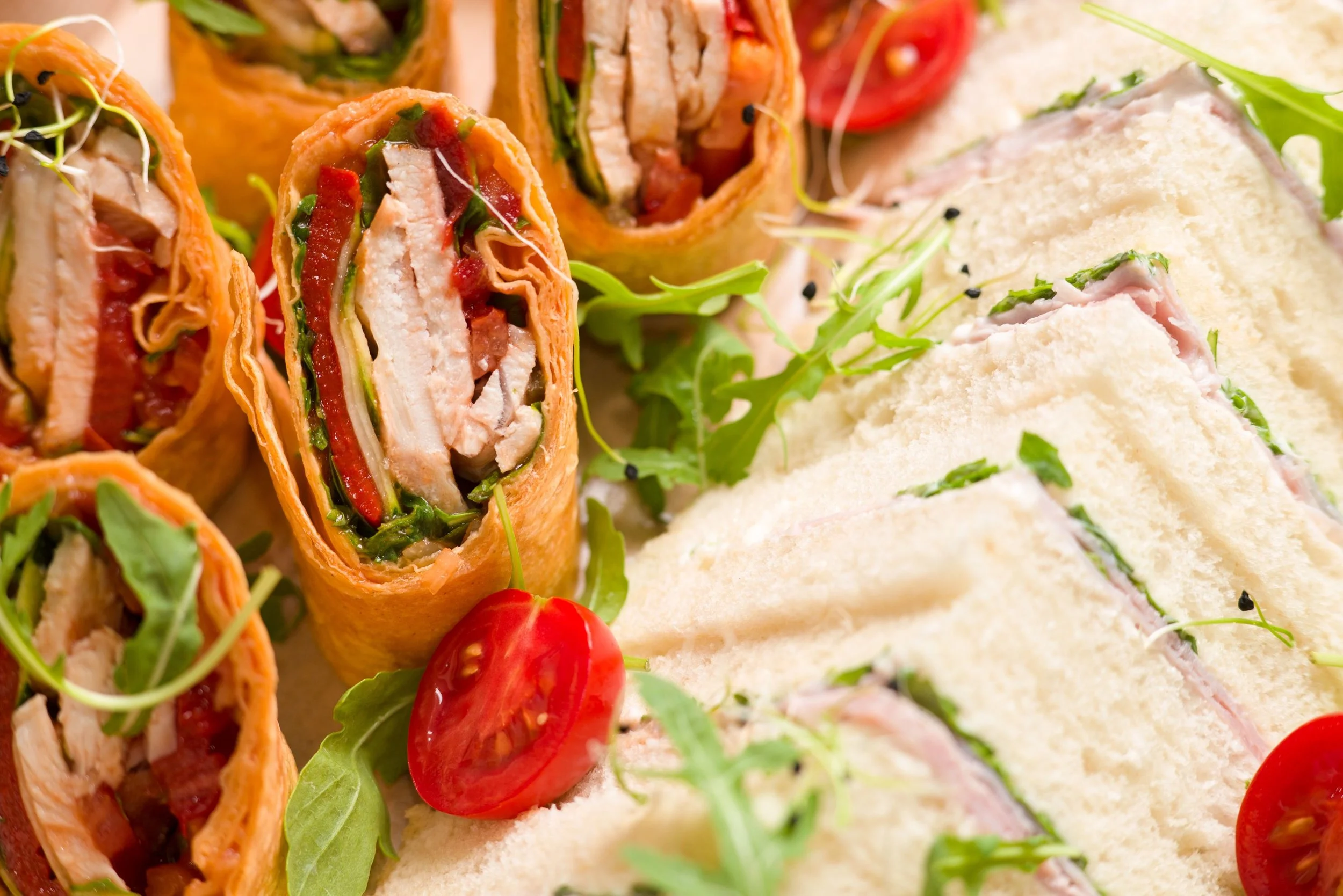Close-up of wraps filled with chicken, vegetables, and sauce, served with cherry tomatoes and greens.