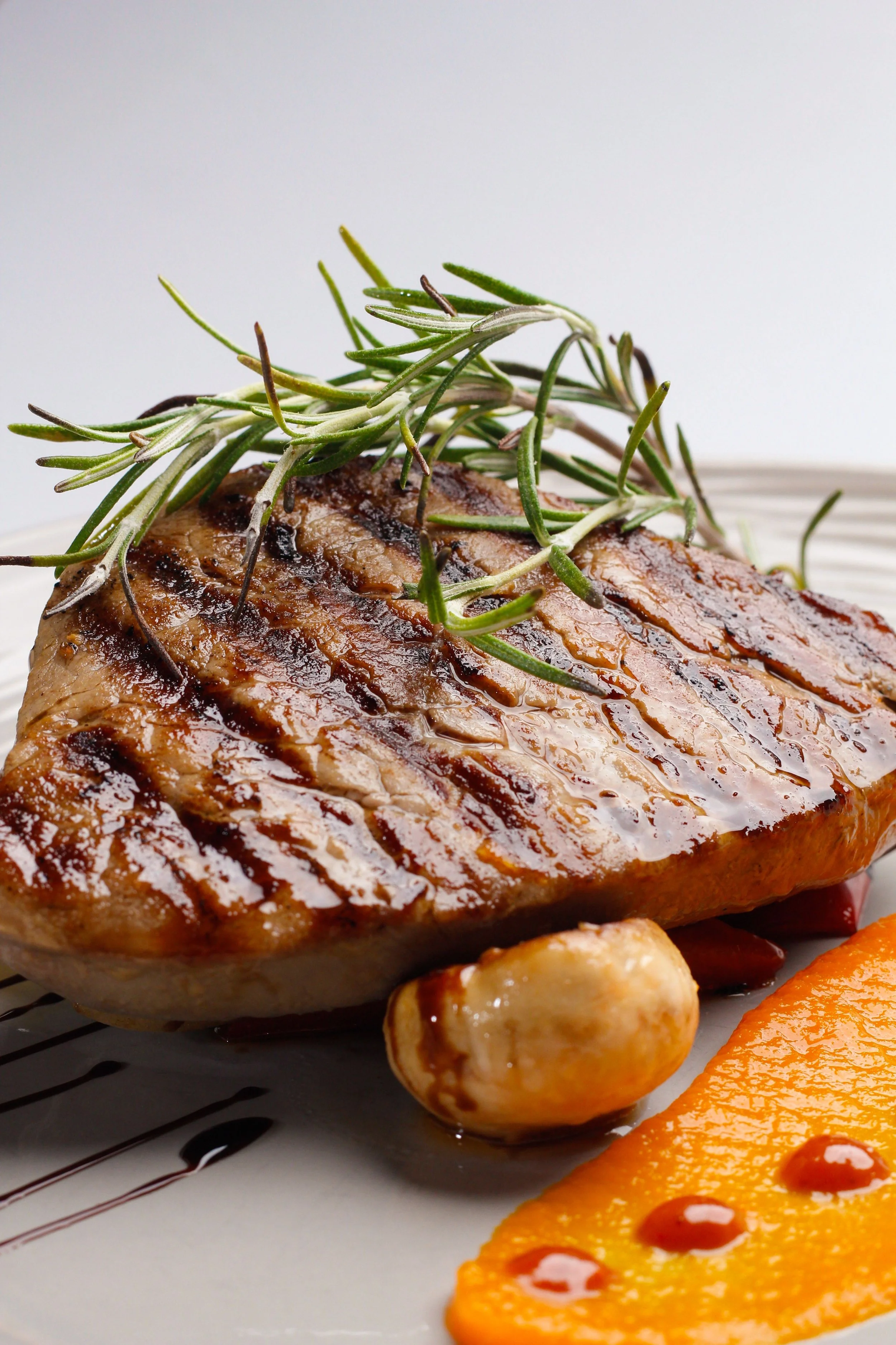 A cooked steak topped with fresh rosemary, with grilled vegetables including carrots and potatoes on a plate.