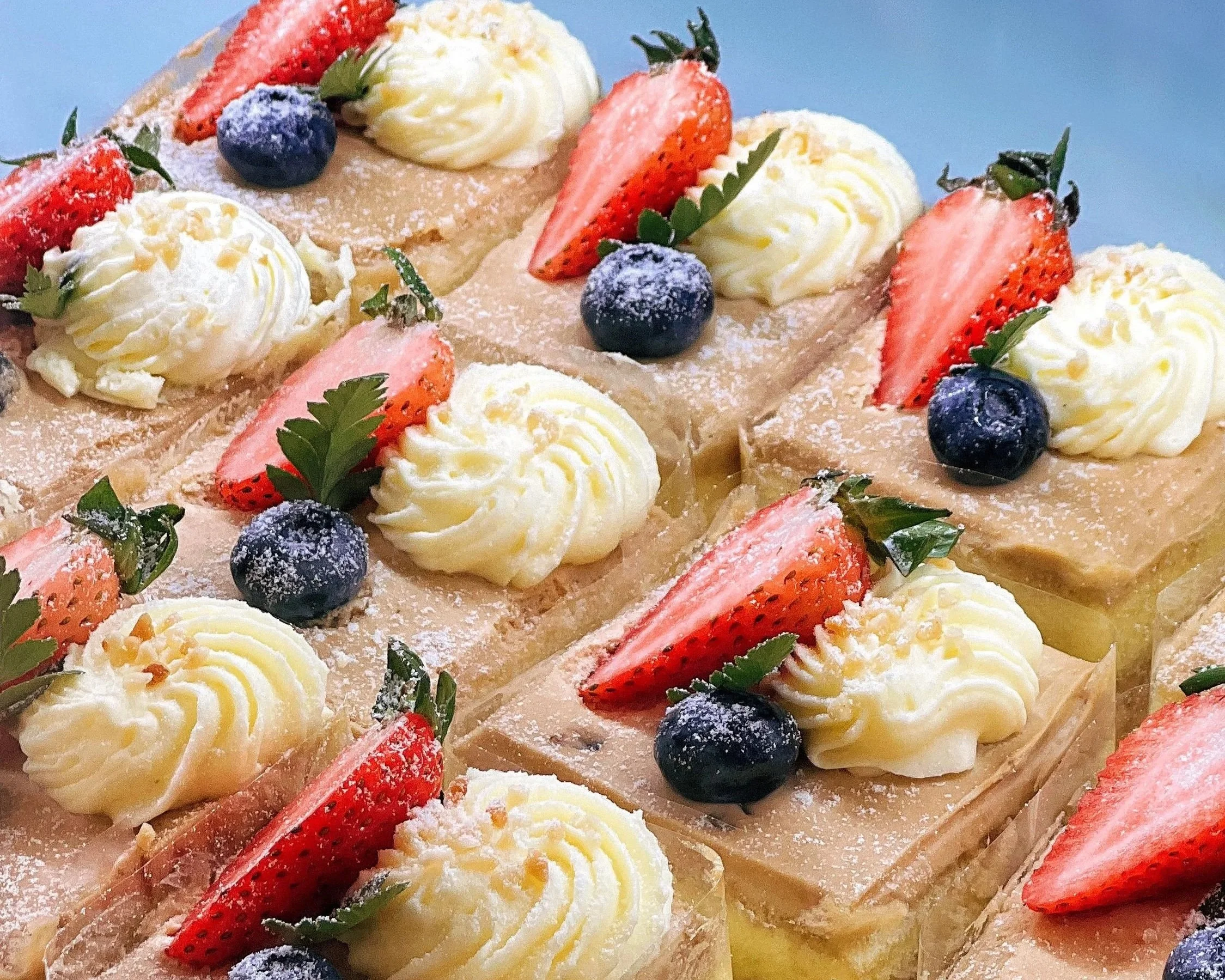 A close-up of a dessert with sliced strawberries, blueberries, whipped cream, green leaves, and dusted powdered sugar.