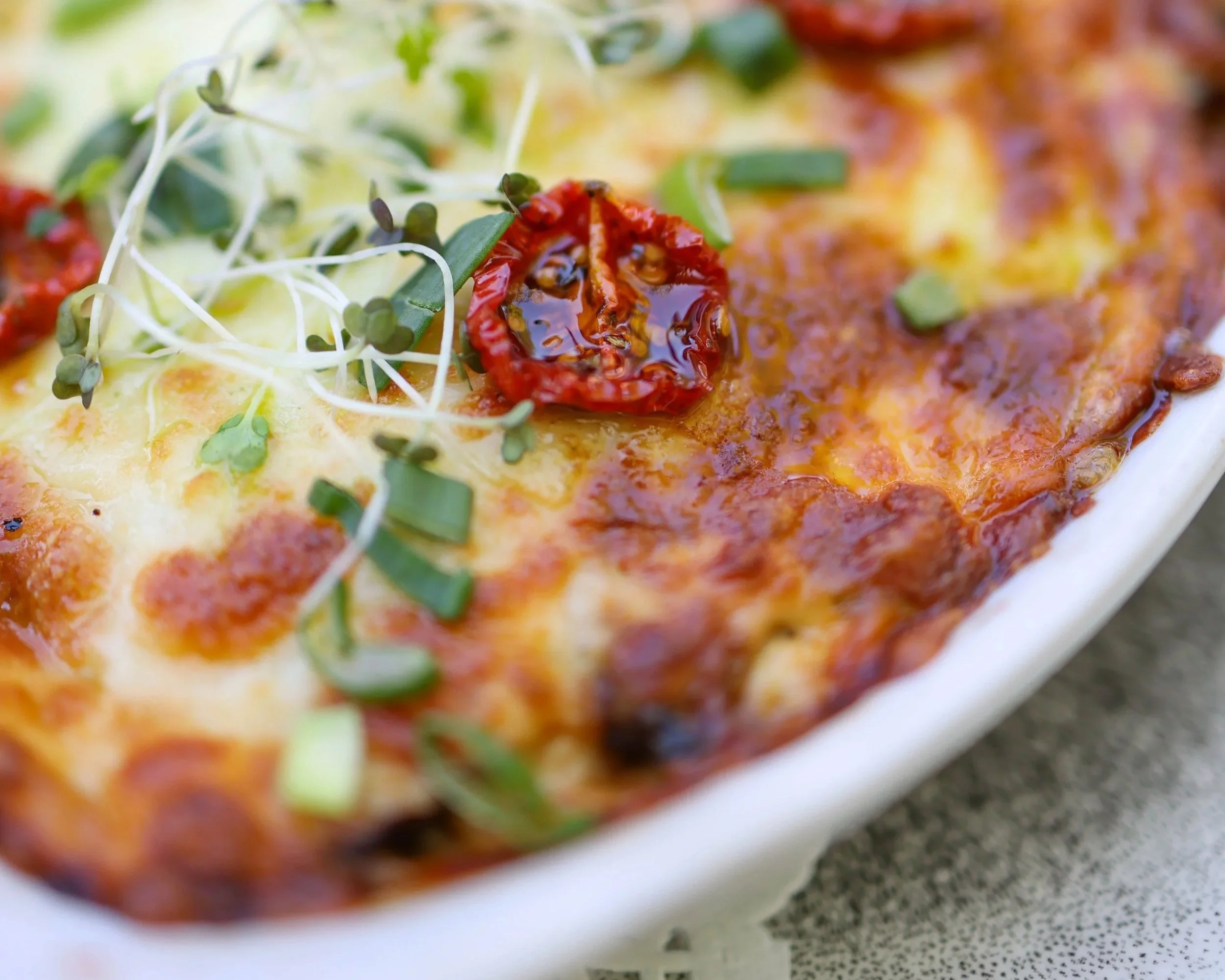 Close-up of a dish with red peppers, green sprouts, and melted cheese or sauce.