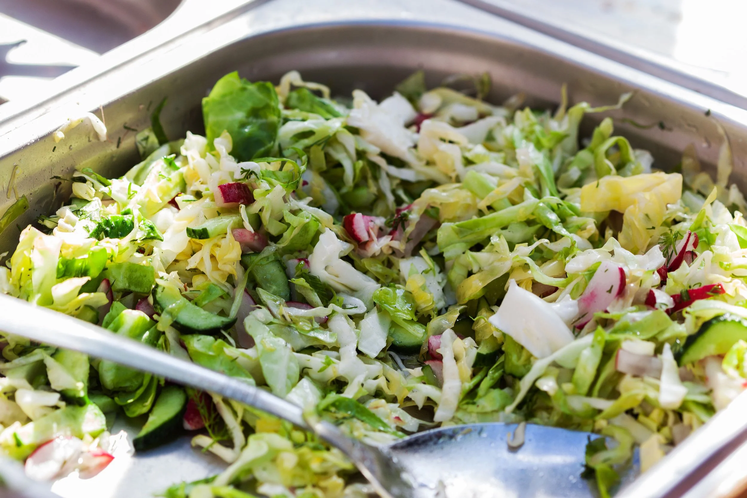 A colander filled with chopped green and red vegetables, possibly for a salad or preparation.