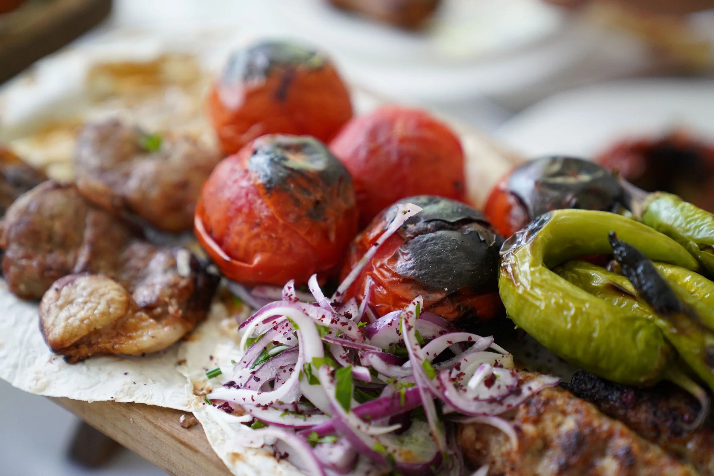 Close-up of an assortment of grilled vegetables on flatbread, including cherry tomatoes, green peppers, and onions, with some herbs and seasoning.